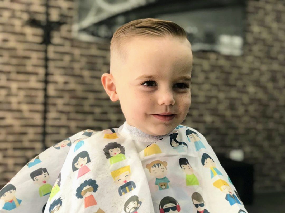 Young boy smiling after a haircut, wearing a kids' cartoon cape