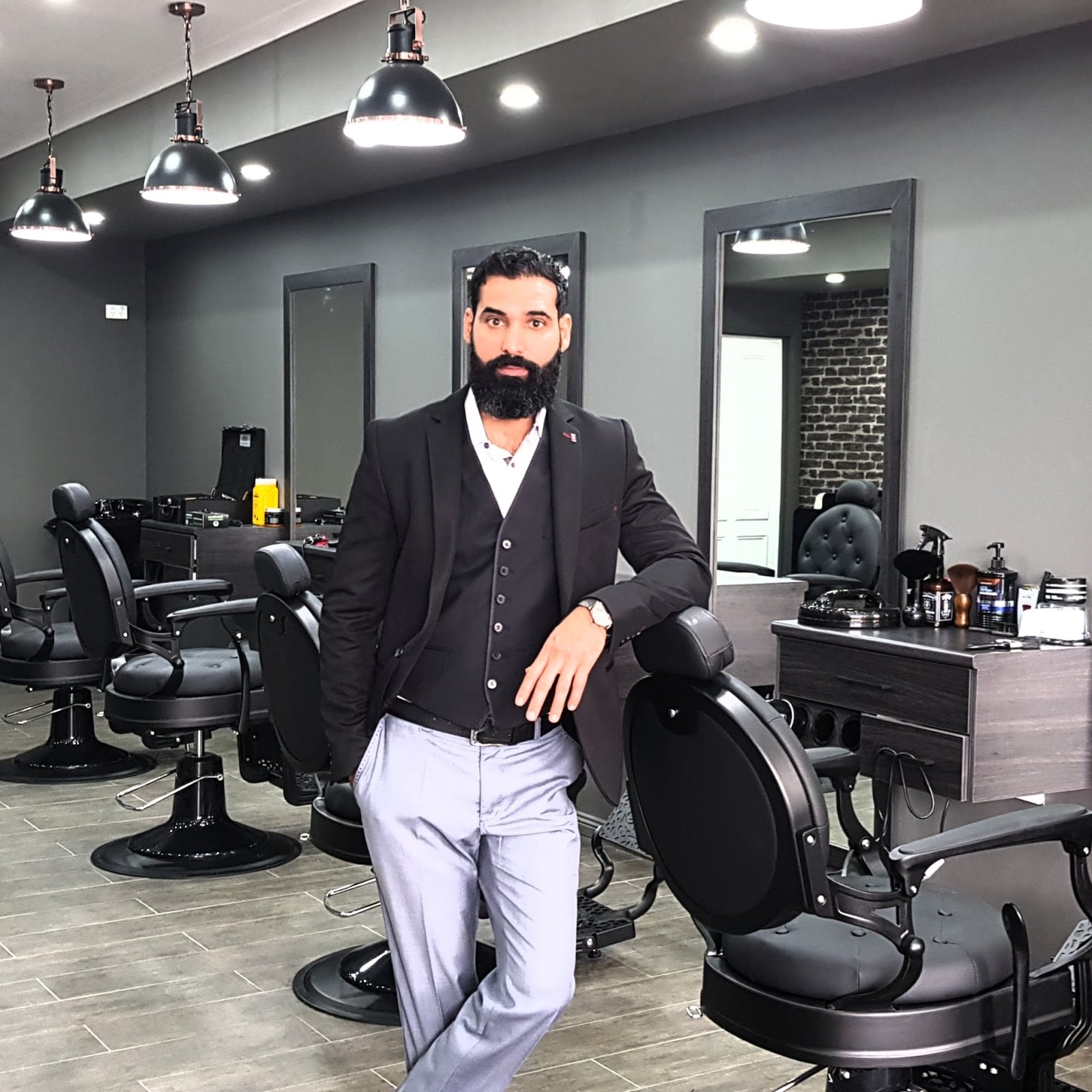 A barber in a dark suit and waistcoat leaning on a chair inside the shop