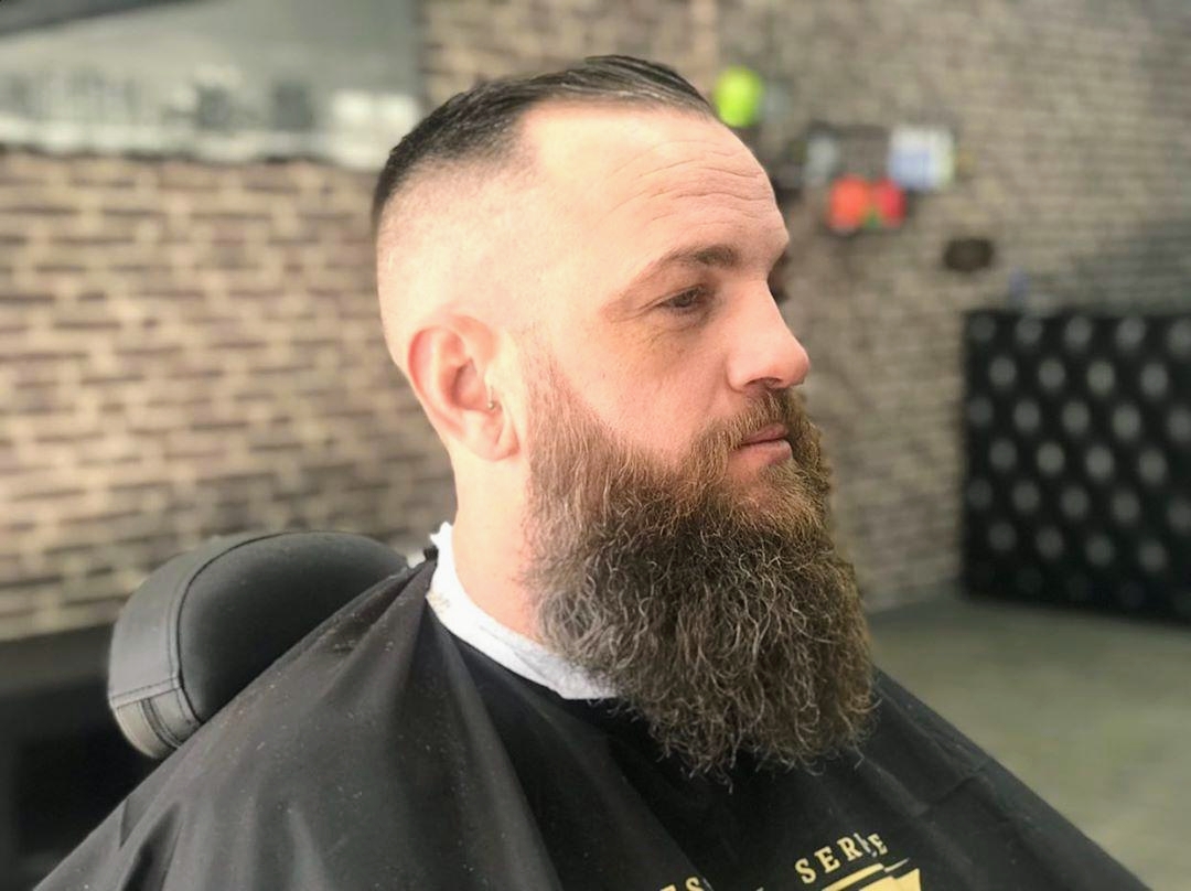 Customer with a long full beard and short sides in a black barber cape