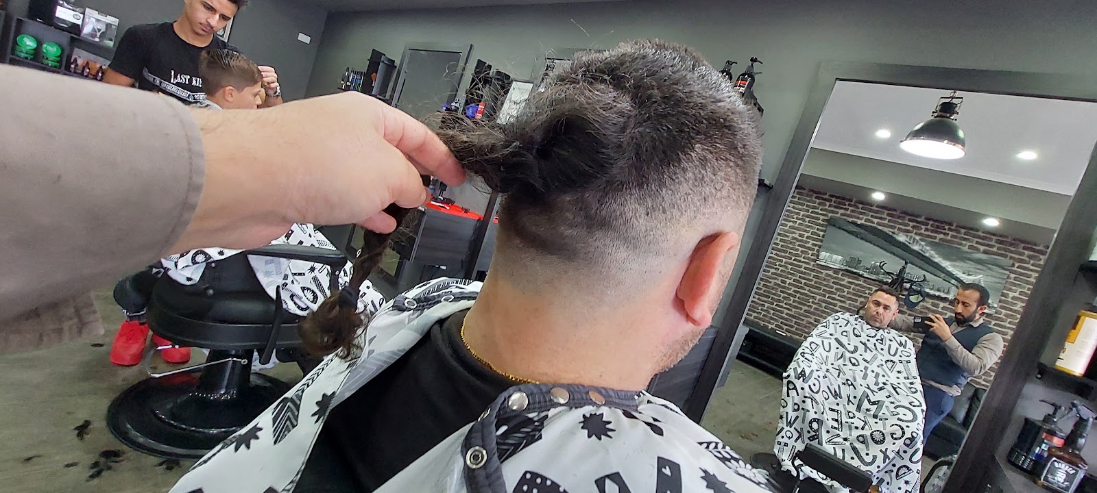 A barber working on an undercut with the hair tied up, mirrors and chairs behind